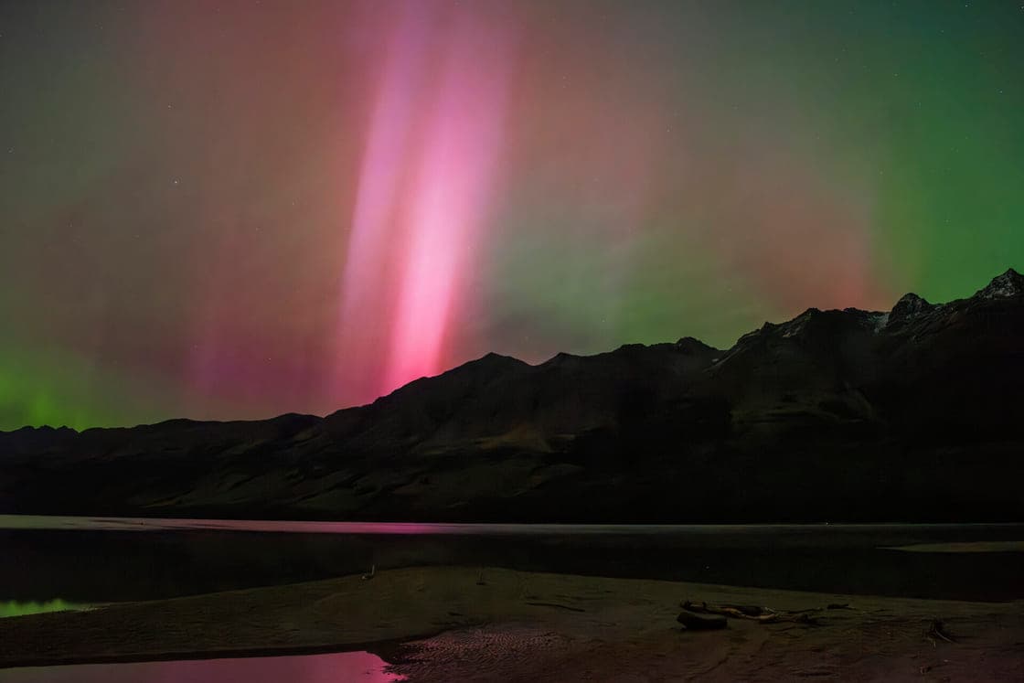 An aurora over the mountains at the head of Lake Whakatipu, pink columns rising into a green sky